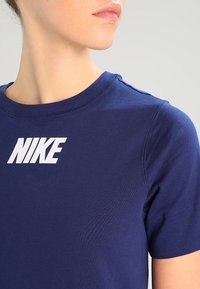 Mörkblå bomulls t-shirt med rund halsringning, med en stor vit "NIKE" logotyp på framsidan och korta ärmar. Slät textur.