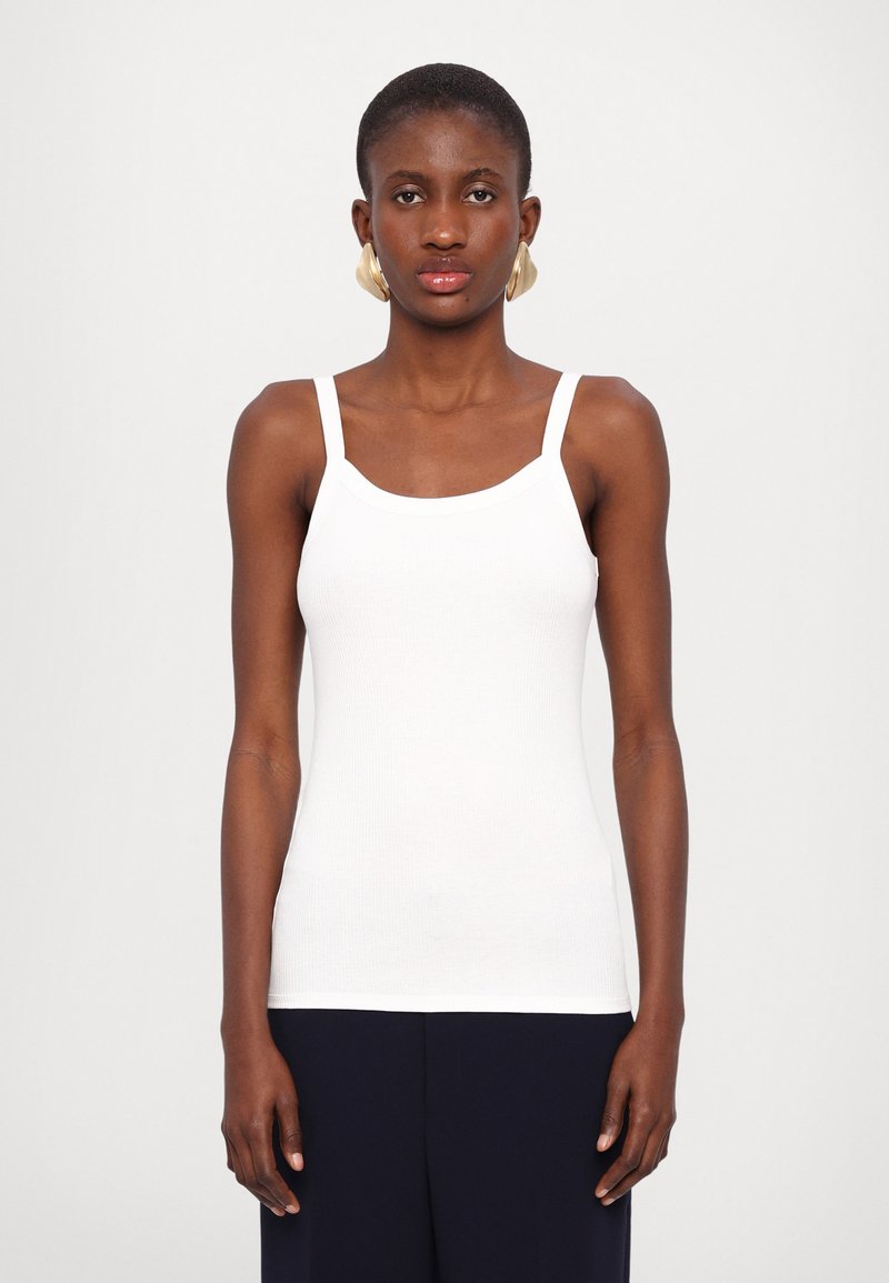 Hvit ribbet tanktop med tynne stropper, med en dyp utringning og en tettsittende silhuett. Stoffet ser glatt og lett ut.