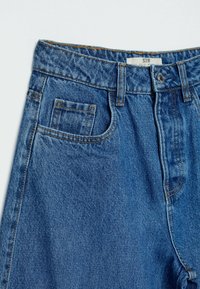 Sininen farkkuhousut, joissa on korkea vyötärö, perinteinen viiden taskun muotoilu ja näkyvät saumat ompeleet. Kankaan pinta on teksturoitu.