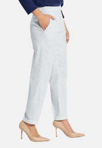 Witte taps toelopende broeken met zijzakken, elastische tailleband en opgerolde manchetten. Gecombineerd met lichtbeige hoge hakken.