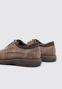 Zapatos de ante marrón con cordones y detalles en cuero marrón oscuro, puntera redonda, superficie texturizada y suela de goma en contraste.