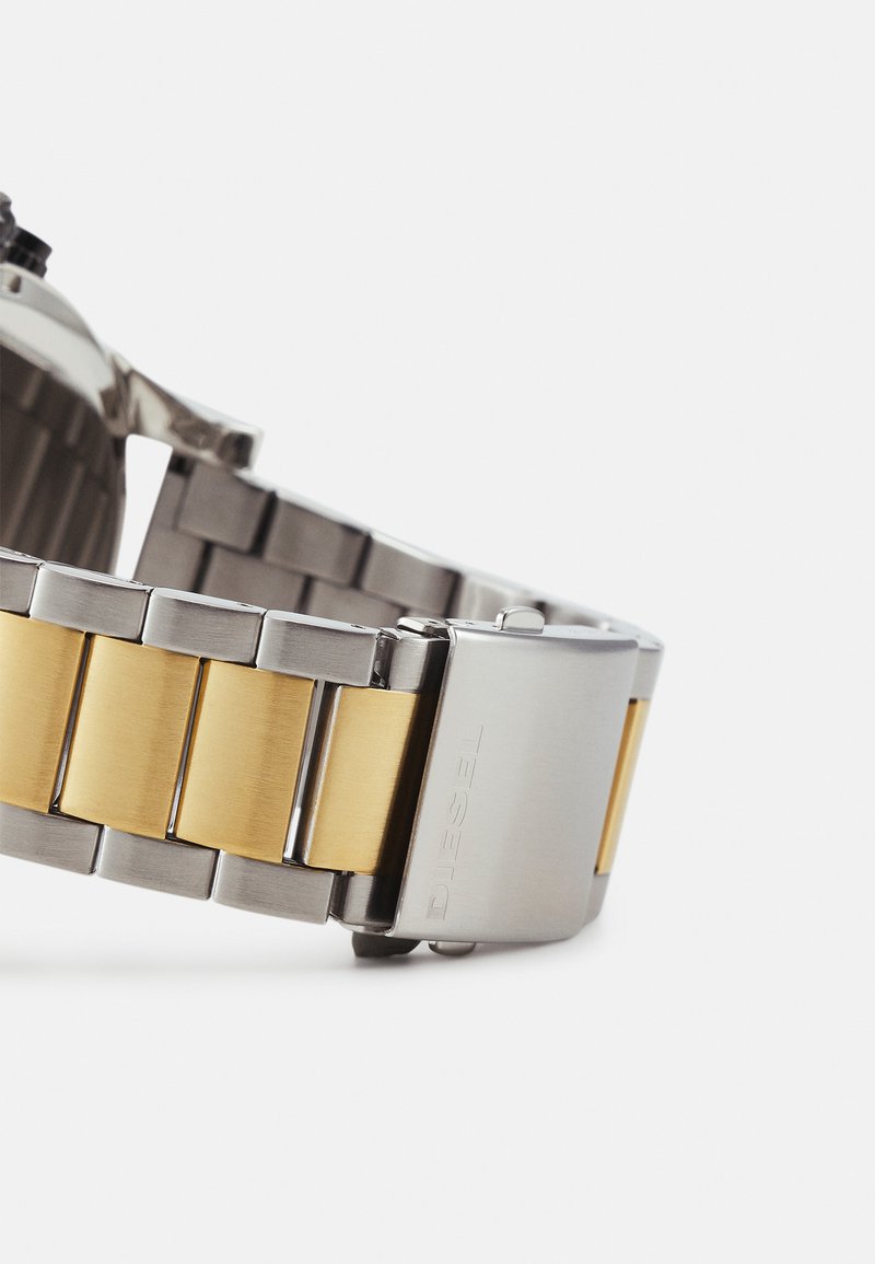 Silberne und goldene Edelstahl-Uhrenarmband mit gebürsteten und polierten Gliedern sowie einer rechteckigen silbernen Schließe, die mit "DIESEL" geprägt ist.