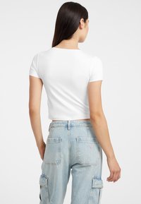 Biała krótka koszulka z krótkim rękawem, w połączeniu z jasnoniebieskimi dżinsami cargo z kieszeniami naszytymi i etykietą z logo z tyłu.