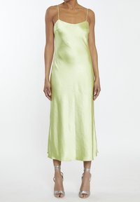 Abito midi in satin verde chiaro, senza maniche, con spalline sottili. Tessuto morbido e silhouette dritta. Sandali argentati con cinturini.