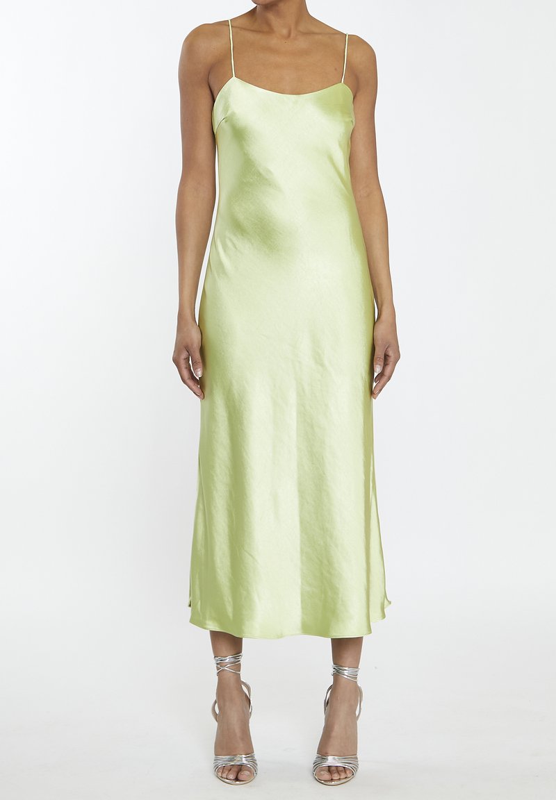 Abito midi in satin verde chiaro, senza maniche, con spalline sottili. Tessuto morbido e silhouette dritta. Sandali argentati con cinturini.