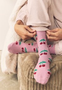 Vaaleanpunaiset sukat, joissa on punaisia ja vihreitä kirsikkakuvioita. Kangas on pehmeää ja kuvioissa on tasaisesti sijoiteltuja kirsikoita ja lehtiä.