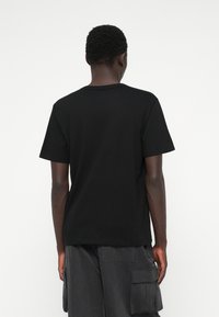 Czarny bawełniany t-shirt z okrągłym dekoltem, krótkimi rękawami i luźnym krojem, wyeksponowany z tyłu. Teksturowana tkanina.