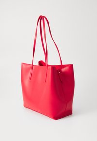 Bolsa tote de couro vermelho com alças longas e finas, textura lisa, design de abertura superior e detalhes mínimos. Adequada para uso diário.