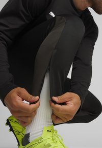 Schwarze Sporthosen mit einem seitlichen Reißverschluss, kombiniert mit leuchtend gelben Sportschuhen und weißen gerippten Socken. Glattes und passgenaues Design.