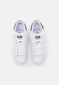 Vita lädersneakers med en slät textur, utrustade med en svart h älflik och klassisk snörning. Märkning finns på tungan.