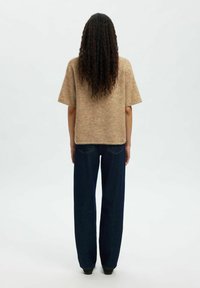 Haut en tricot beige à manches courtes, associé à un jean large bleu marine. La tenue présente une coupe décontractée et un tissu texturé.