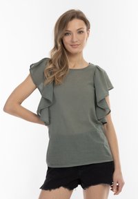 Olivenfarvet, løst tilpasset bluse med korte, flæseærmer og rund halsudskæring. Blødt, let stof. Kombination med sorte shorts.