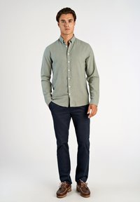 Jasnozielona koszula zapinana na guziki o miękkiej fakturze, zestawiona z granatowymi spodniami i brązowymi mokasynami. Prosty wzór o klasycznym kroju.