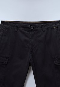 Schwarze Cargo-Hose aus Baumwolle mit flacher Vorderseite, zwei Seitentaschen, Knopfverschluss und Kontrastnähten am Bund.