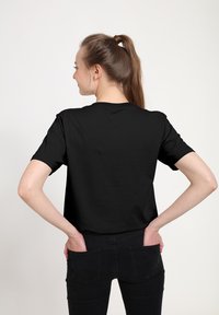 Svart t-shirt med kort ärm och rund halsringning, slät textur och avslappnad passform. Buren tillsammans med mörka denimjeans, vilket ger en avslappnad och minimalistisk stil.