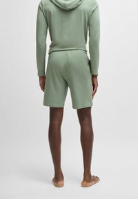 Lichtgroene capuchontrui en korte broek gemaakt van zacht stof, met een losse pasvorm en een elastische tailleband, gezien van achteren.