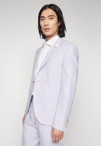 Helles Lavendel-Leinenanzug mit einreihigem Jacket, Reverskragen und hellblau gestreifter Hemd. Mit Knopf-Akzenten an den Ärmeln.