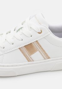 Weißer Ledersneaker mit goldenen und beigen Streifen, weißen Schnürsenkeln und Logodetail. Verfügt über eine strukturierte Gummisohle und abgestickte Akzente.