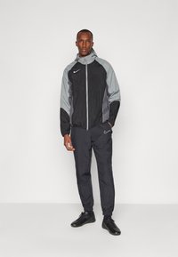 Survêtement Nike comprenant une veste noire avec des accents gris, fermeture éclair et capuche ; joggeurs noirs avec bas élastiques et logo.