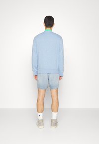 Ljusblå sweatshirt med grön krage, kombinerad med ljusa denimshorts. Modellen har på sig grå högskor och vita ankelsockor.