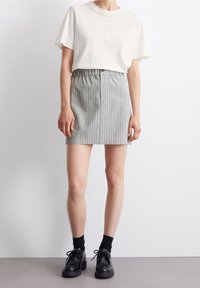 Camiseta blanca de manga corta combinada con una falda corta a rayas grises, que presenta una cinturilla elástica. Unos zapatos negros de cordones y calcetas al tobillo completan el look.
