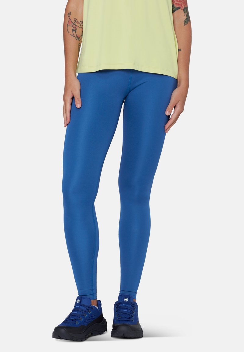 Personne portant des leggings bleu vif, des chaussures de sport bleues et un haut jaune clair, debout avec les mains détendues le long du corps.