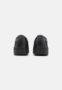 Chaussures en cuir noir avec une tige lisse, un talon arrondi, une semelle texturée et un design minimaliste. Présence de coutures le long du bord.