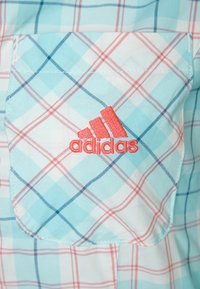 Hellblau- und weißkariertes Stofftasche mit rotem, gesticktem Adidas-Logo, das zentriert auf der Tasche angebracht ist.