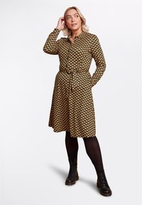 Abito camicia a maniche lunghe con uno sfondo nero e motivi floreali gialli, vita cintrata e tasche, abbinato a stivali combat neri.
