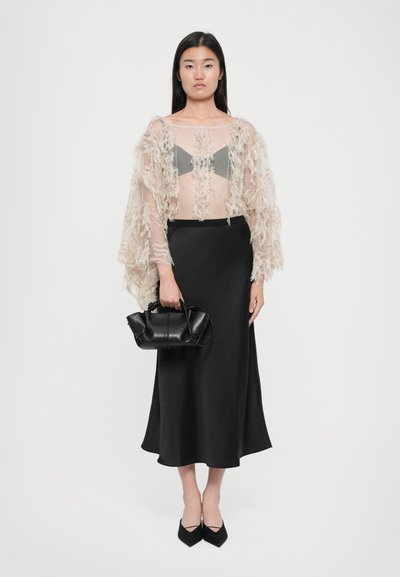 Beige textured shawl with fringes over a gray bralette and black satin midi skirt. Black handbag and pointed black shoes complete the look.