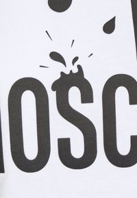 Černá stylizovaná skvrna nad písmenem "S" v tučném černém textu "MOSC" na bílém textilním pozadí.