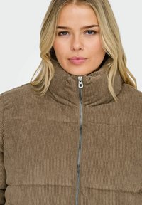 Smeđa kordsurova jakna s visokim ovratnikom i zatvaračem, s prošivenim dizajnom i rebrastom teksturom.