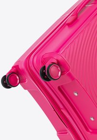 Maleta rígida de color rosa brillante con surcos texturizados, ruedas dobles giratorias y cierre de cremallera. Presenta acentos negros en las ruedas.