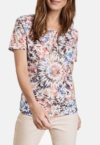 Camisa de manga corta con un patrón geométrico multicolor, con un fondo crema y acentos en rosa, azul y negro. Textura de tela suave.