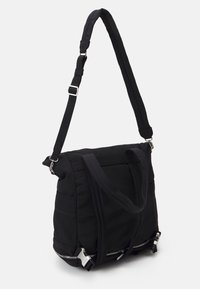 Sac à dos en nylon noir avec bretelle d'épaule rembourrée et réglable, poignées supérieures, multiples fermetures éclair et poches latérales sur fond blanc.