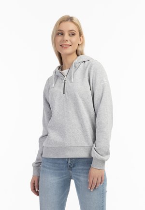 Felpa grigia realizzata in materiale morbido con zip frontale e coulisse. Presenta polsini a costine e un logo sulla manica. Indossata con jeans azzurri chiari.
