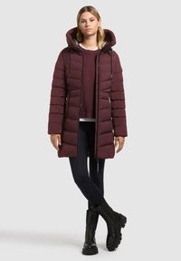 Mørkerød polstret jakke med hætte, lynlås og snoretræk. Bæres over en mørk sweater og leggings. Sorte chunky støvler fuldender looket.