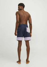 Pantaloni da nuoto blu navy con un pannello viola all'orlo e una tasca posteriore. Materiale leggero con vestibilità comoda e vita elastica.