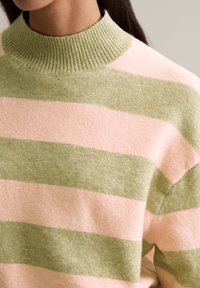 Gestreifter Pullover mit hellrosa und grünen Farbtönen, einem gerippten hohen Kragen und einer weichen Textur. Auffällige breite horizontale Streifen.