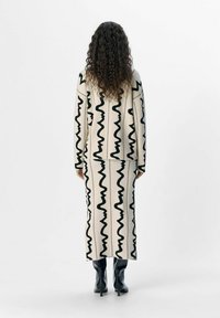 Beżowy sweter i spódnica midi w zestawie z czarnymi wzorami w zygzak, połączone z czarnymi kozakami do kolan. Miękka tekstura i luźny fason.
