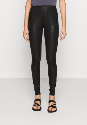 Black leggings featuring a textured snake pattern, high waistband, and a sleek, form-fitting design. Paired with black strappy sandals.