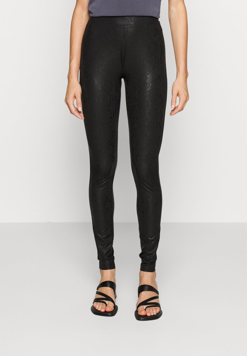 Svarta leggings med ett texturerat orm-mönster, hög midja och en glansig, kroppsnära design. Matchade med svarta sandaler med remmar.