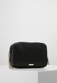 Borsa a tracolla in pelle nera con superficie texture, tracolla in catena dorata e chiusura con zip. Presenta un logo del marchio sottile sul davanti.