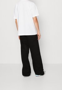 Bílé bavlněné tričko s krátkými rukávy v kombinaci s volnými černými kalhotami. Minimalistický design s hladkou texturou.