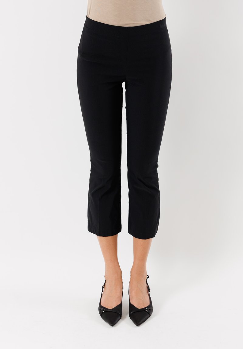 Pantaloni neri cropped realizzati in tessuto elastico con una superficie liscia e una cintura elastica, abbinati a décolleté nere a punta.