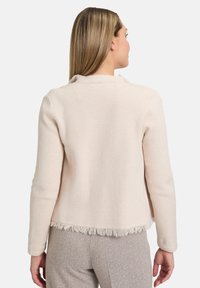 Veste ajustée rose clair avec un ourlet à franges, des manches longues et un col arrondi, fabriquée à partir d'un tissu doux.