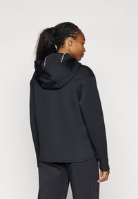 Sudadera negra con un corte relajado, que presenta una capucha con cordón y puños de canalé. Textura suave y detalles en contraste en el cuello.