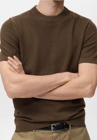 Maglione corto a maniche corte di colore marrone con scollatura rotonda, caratterizzato da un tessuto testurizzato e una vestibilità slim. Abbinato a pantaloni in tonalità neutre e una cintura nera.