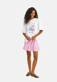 Biely tričko s farebnou grafikou mašle a textom, v kombinácii s rúžovou sukňou. Model má na sebe topánky s leopardím vzorom. Neformálny, uvoľnený strih.