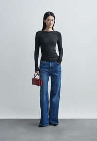 Top preto de manga comprida com riscas, jeans de ganga azuis com perna em sino, a segurar uma pequena mala vermelha. Design simples e casual com uma silhueta ajustada.